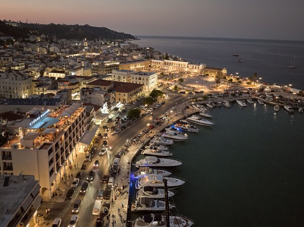 A coastal cityscape with a marina filled with yachts, a prominent building with a clock tower, and a densely packed urban area with visible streets and buildings. - Hotel Strada Marina (Zakynthos)