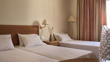 A hotel room with two single beds, a nightstand with a lamp, and a window with curtains.