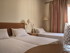 Camera d'albergo con due letti singoli, un comodino con una lampada e una finestra con tende.