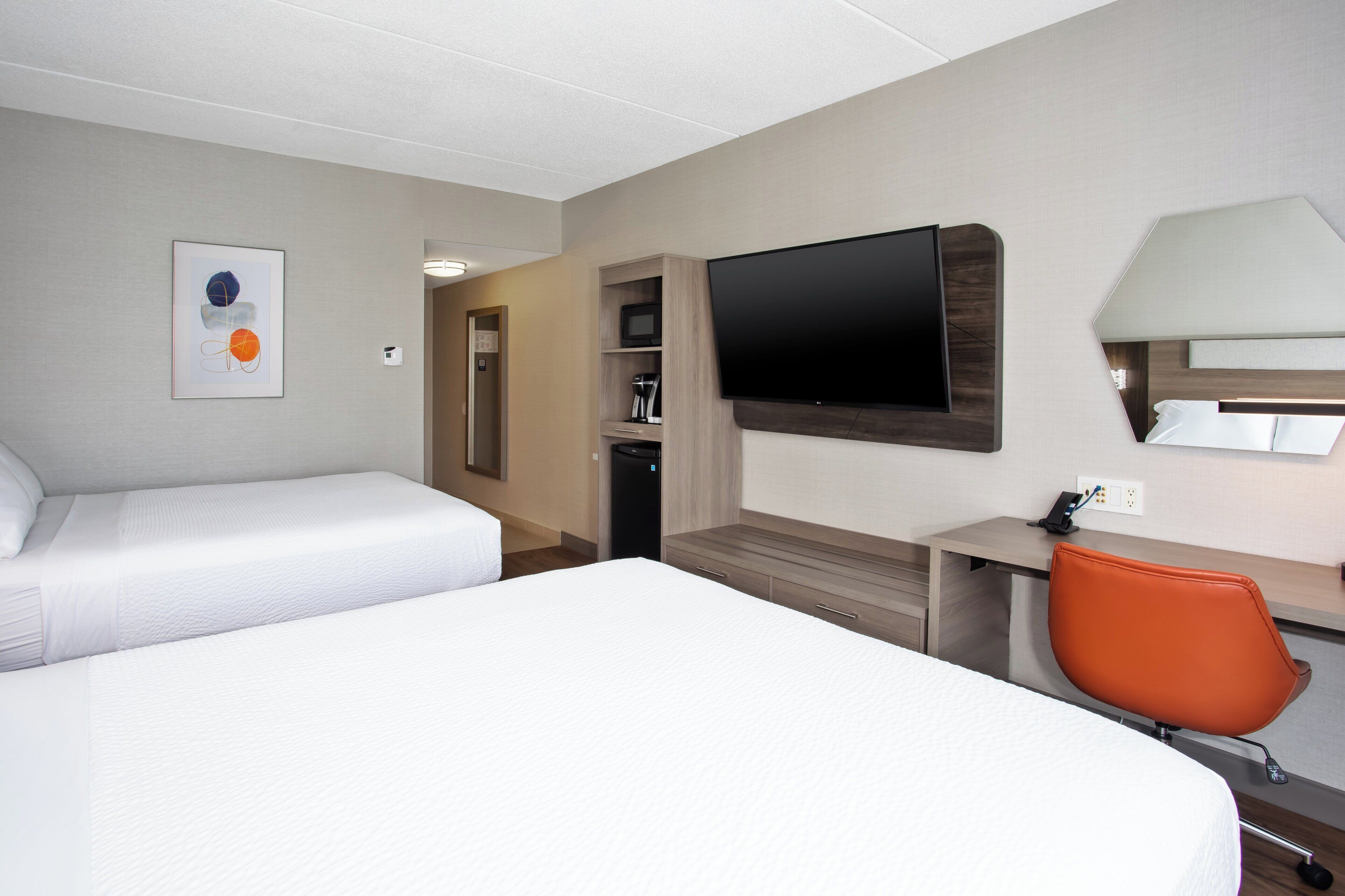 A hotel room with two beds, a TV, a desk with a chair, and a mirror.
