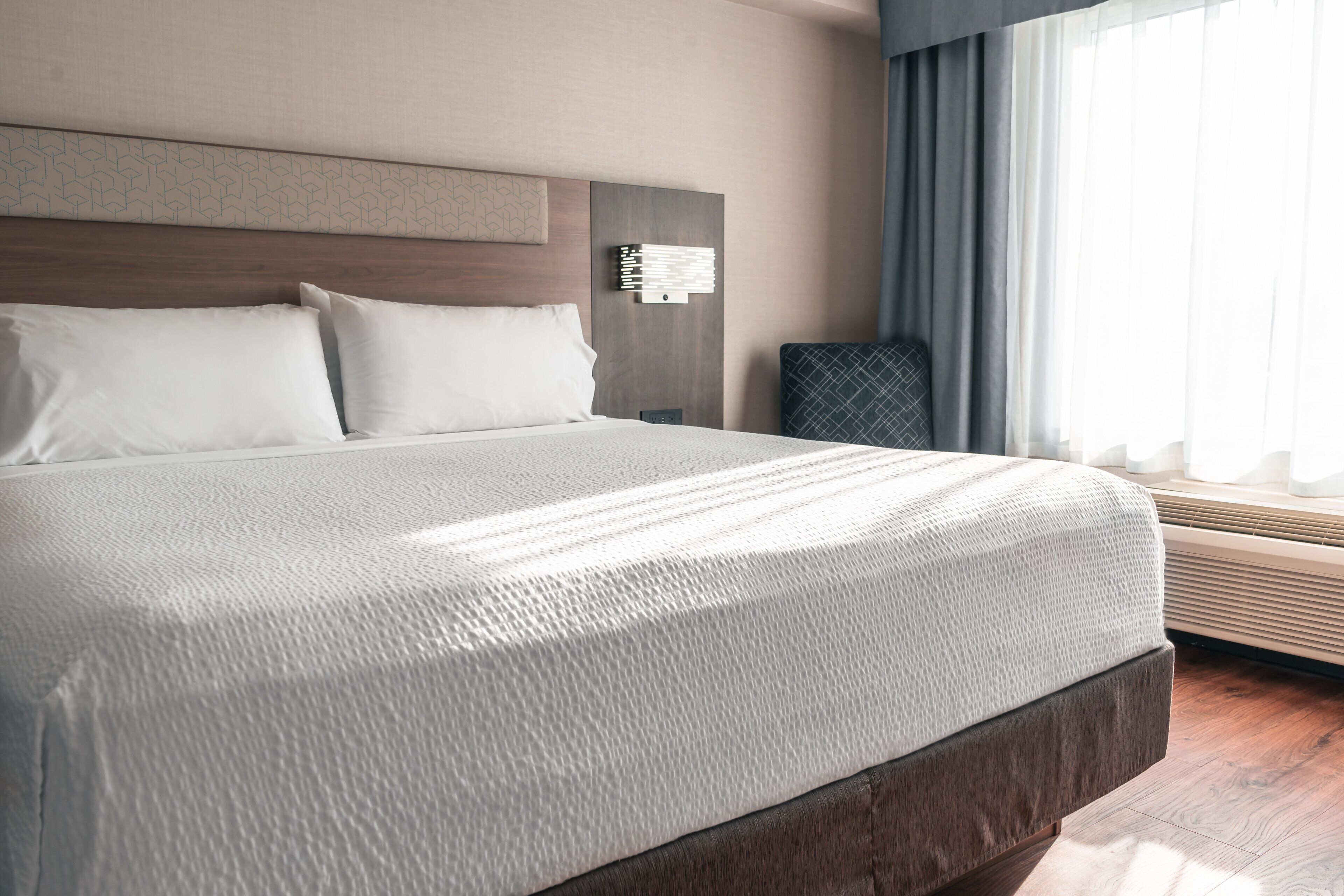 A neatly made bed with a textured white bedspread, a wooden headboard, and a bedside table with a lamp.