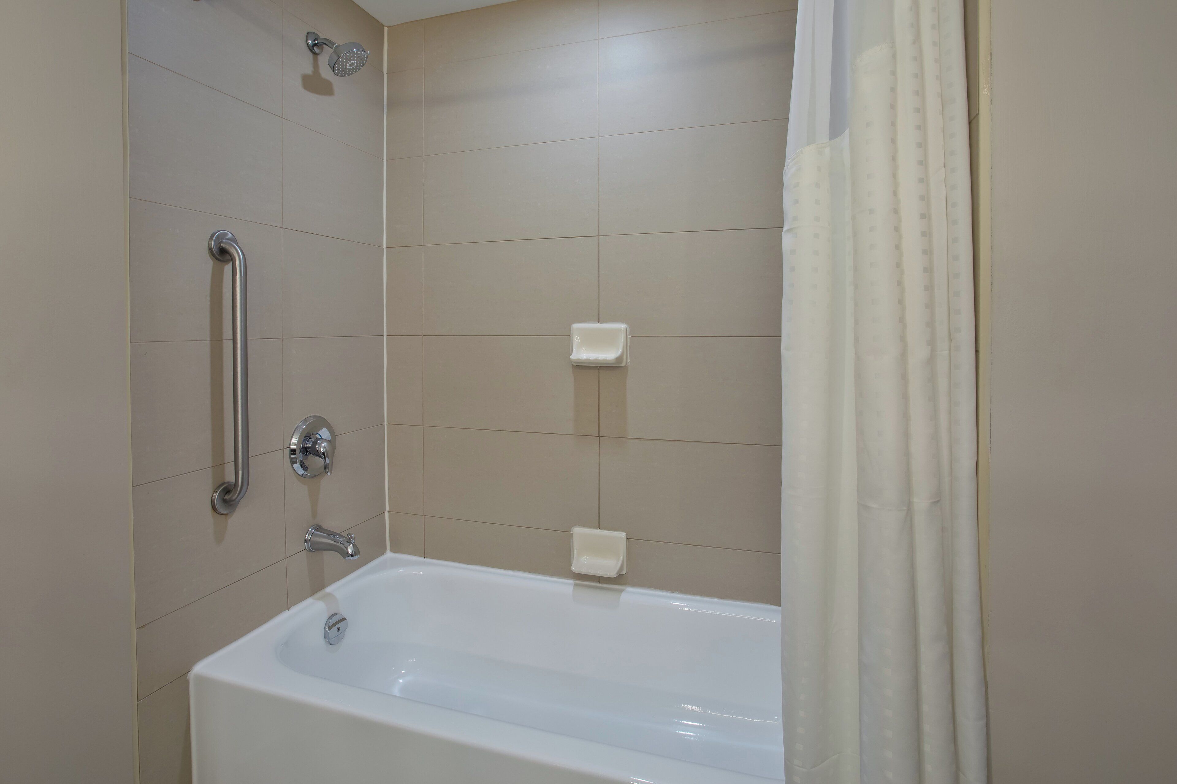 A bathroom with a bathtub, a shower, and a handrail.