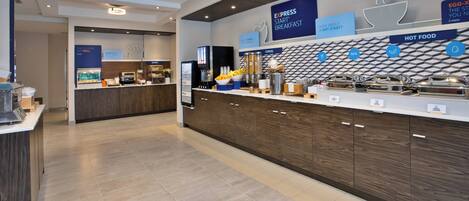 A modern breakfast area with a counter, coffee machines, and a wall displaying breakfast options.
