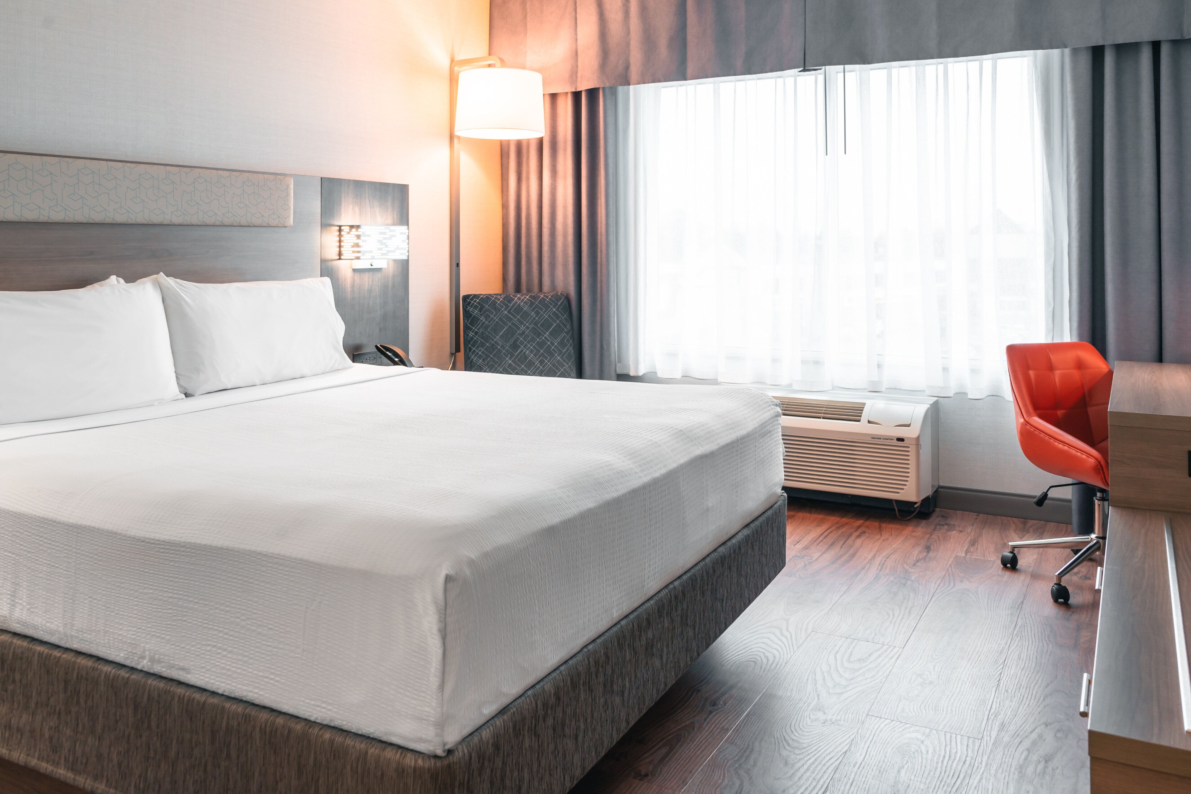 Ein Hotelzimmer mit einem großen Bett, einem Schreibtisch, einem Stuhl und einem Fenster mit Vorhängen.