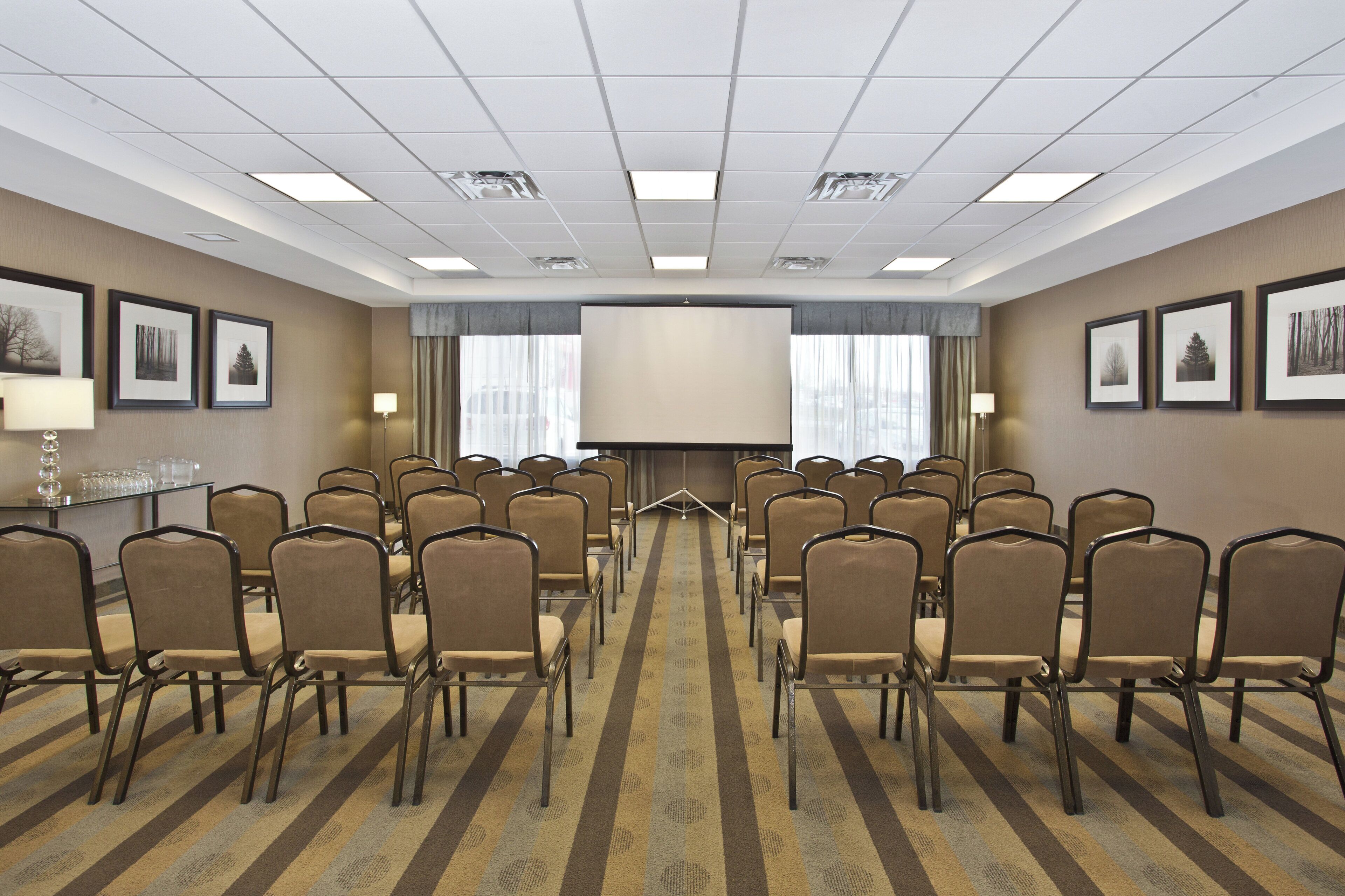 A conference room with rows of chairs, a large screen, and framed pictures on the walls.