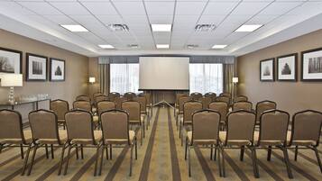 A conference room with rows of chairs, a large screen, and framed pictures on the walls.