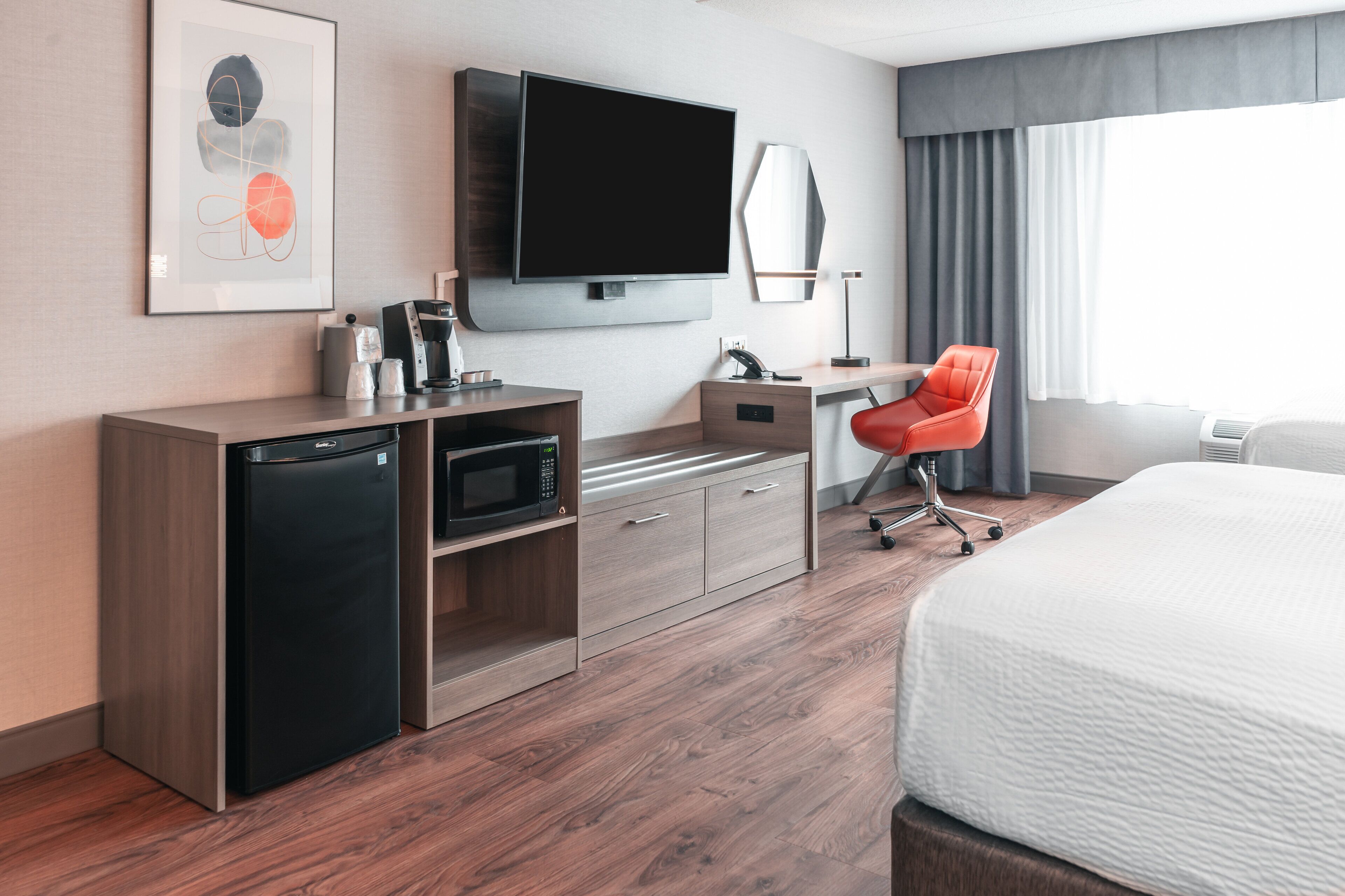 A hotel room with a bed, a desk with a chair, a television, a microwave, and a refrigerator.