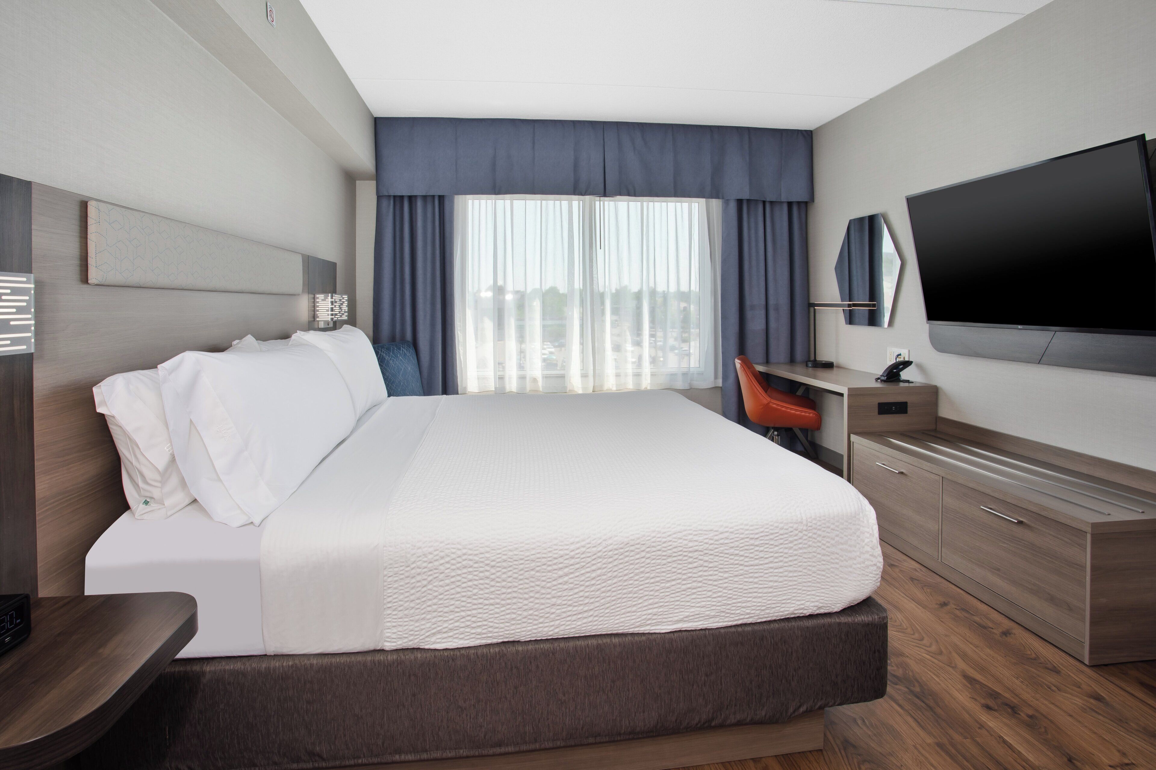 Habitación de hotel moderna con una cama grande, un escritorio, un televisor de pantalla plana y vistas a la ciudad a través de la ventana.