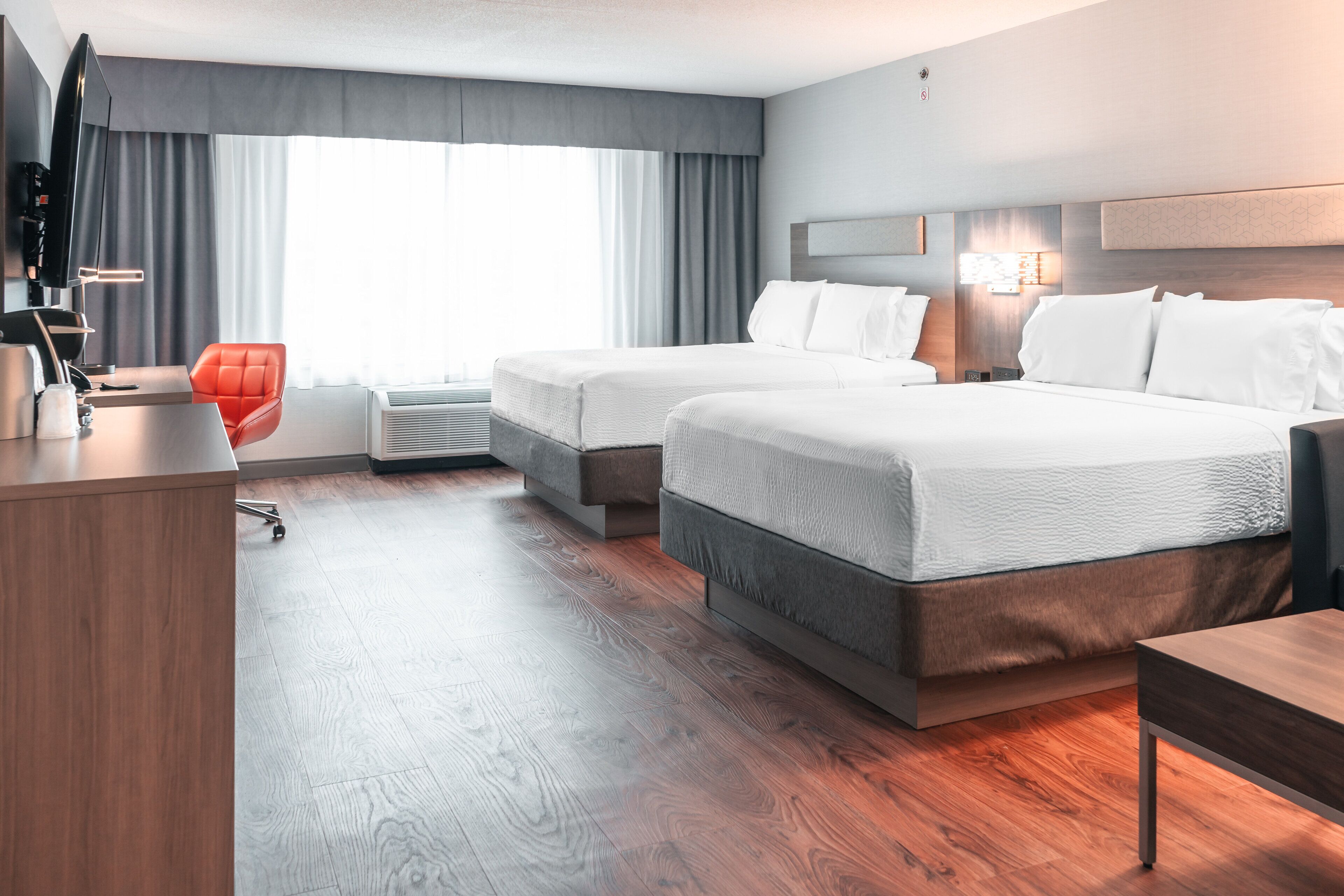 A modern hotel room with two beds, a desk, a chair, and a large window with curtains.