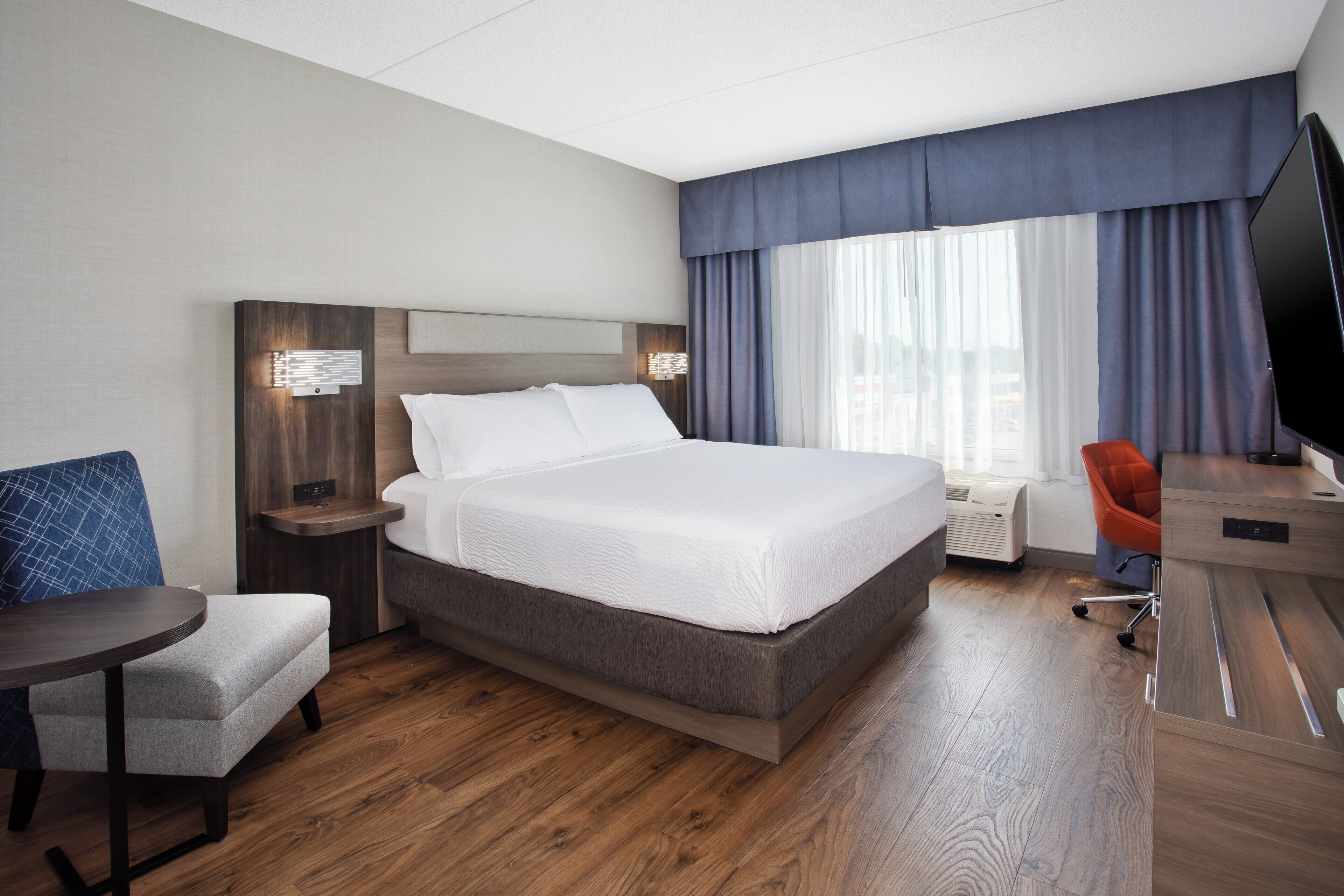Habitación de hotel con una cama grande, un escritorio, una silla, un televisor y una ventana con cortinas.