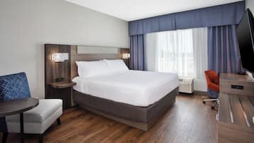 Habitación de hotel con una cama grande, un escritorio, una silla, un televisor y una ventana con cortinas.