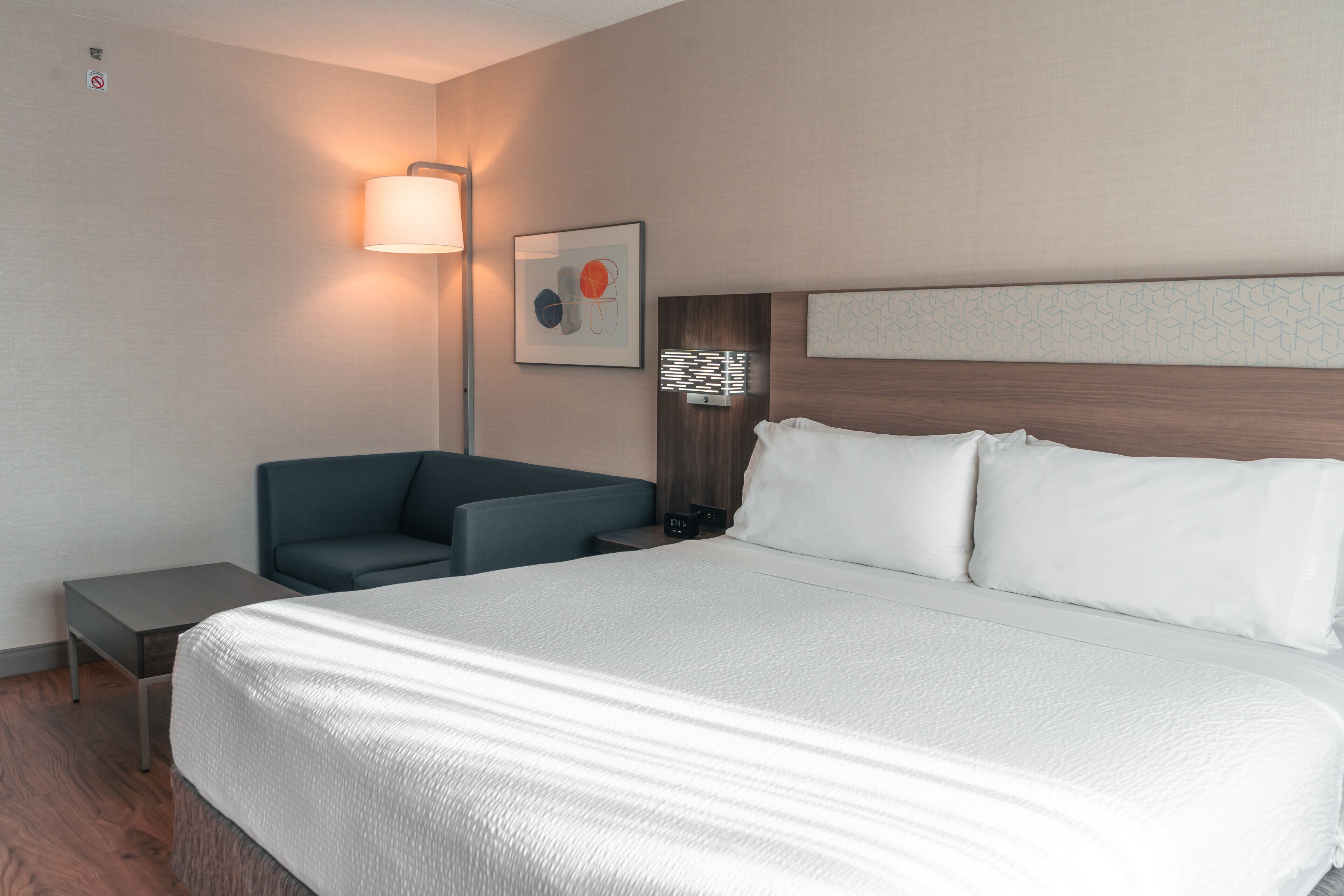 Habitación de hotel con una cama grande, un escritorio, una silla, una lámpara de pared y una obra de arte enmarcada.