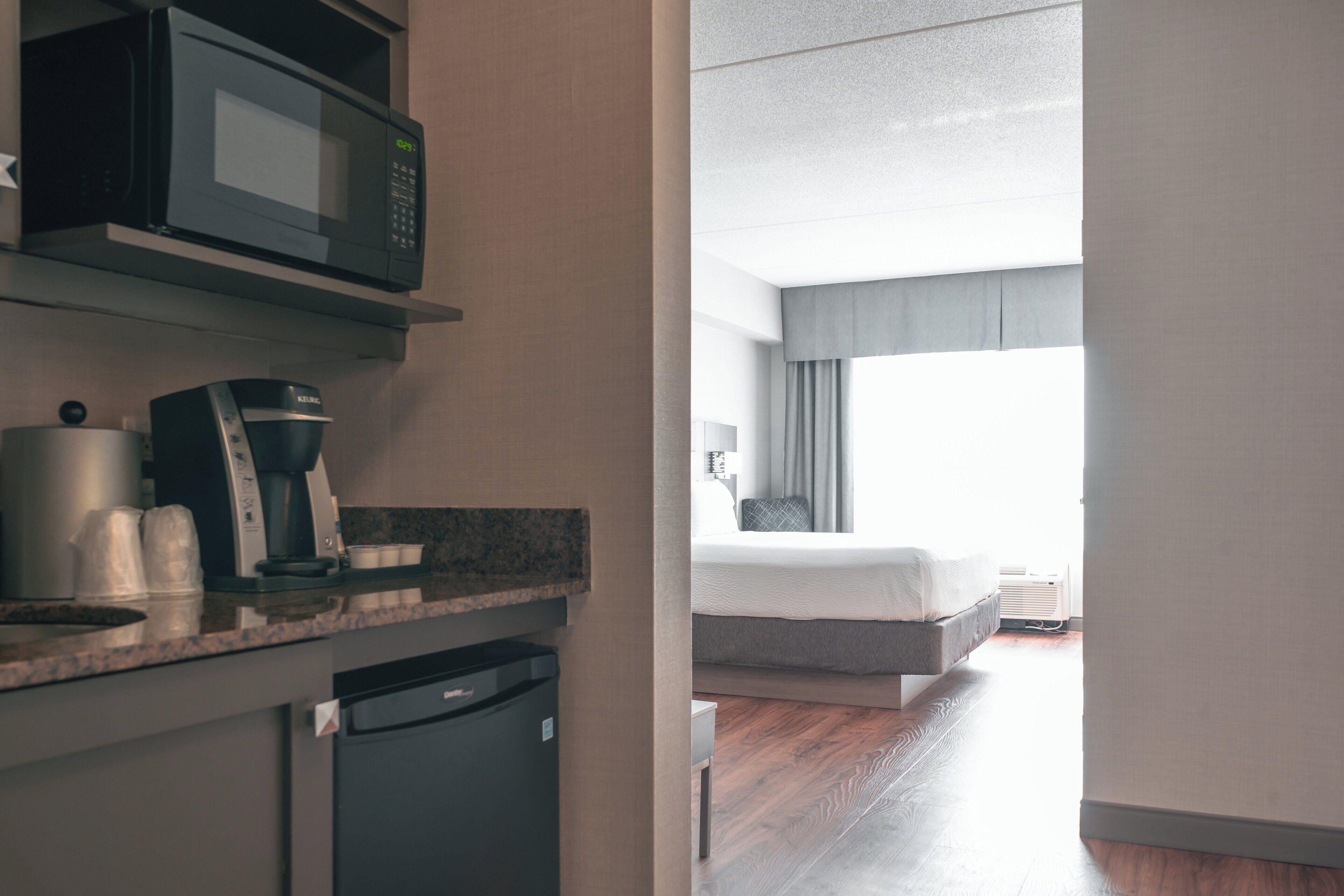 A hotel room with a kitchenette, a bed, and a window with curtains.