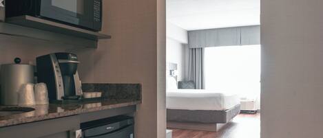 A hotel room with a kitchenette, a bed, and a window with curtains.