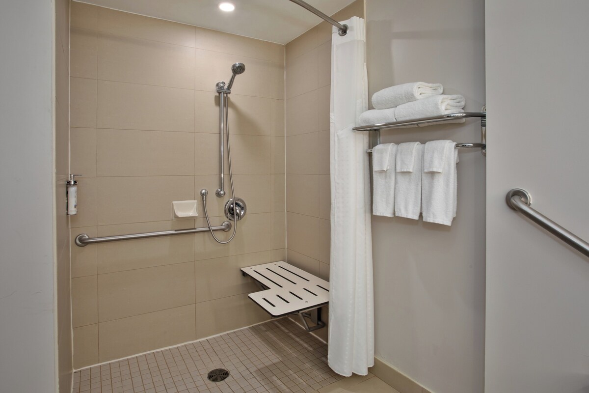A bathroom with a shower, grab bars, a white towel rack, and a white shower curtain.