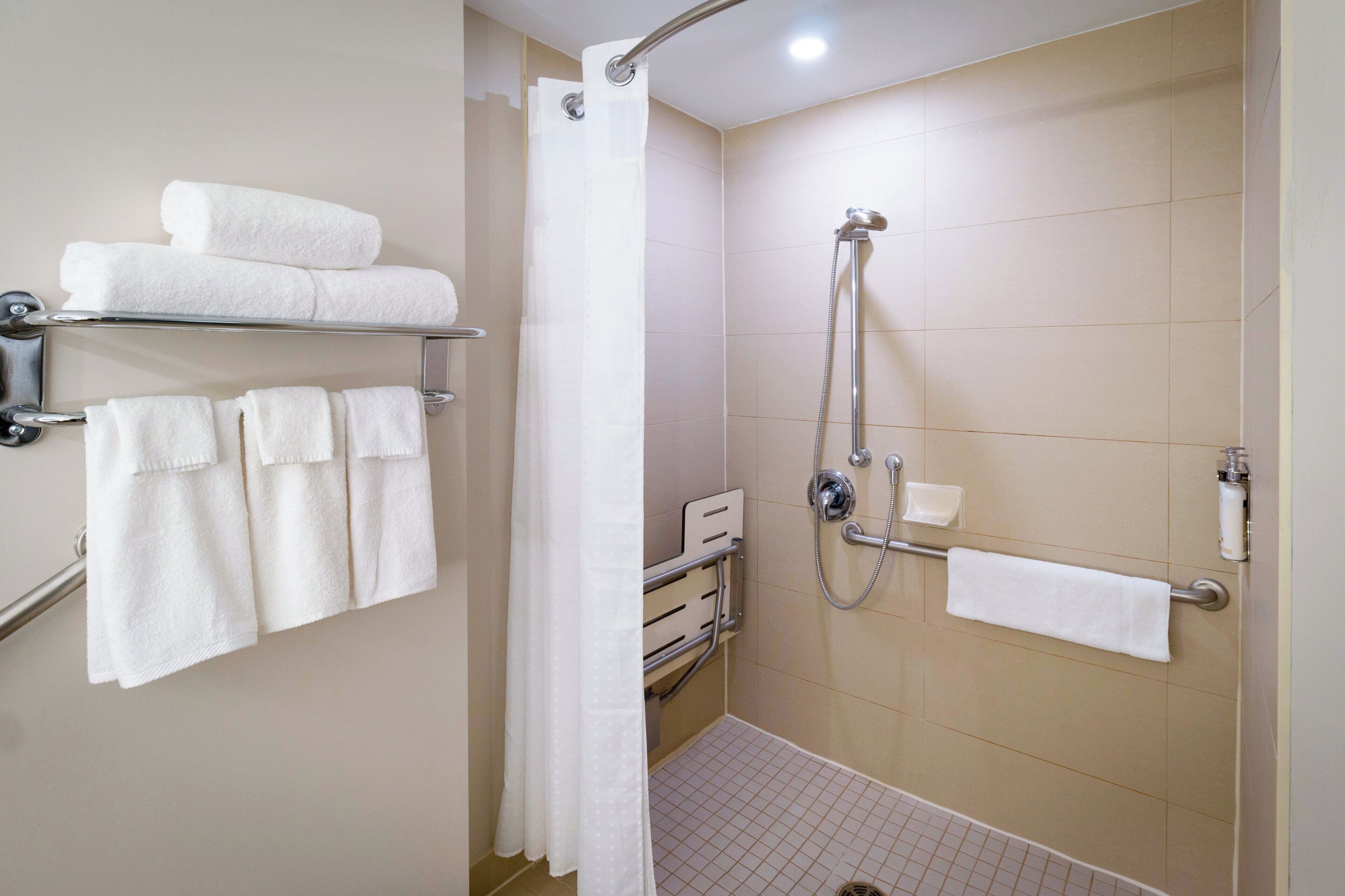 A bathroom with a shower, a towel rack with multiple towels, and a toilet paper holder.