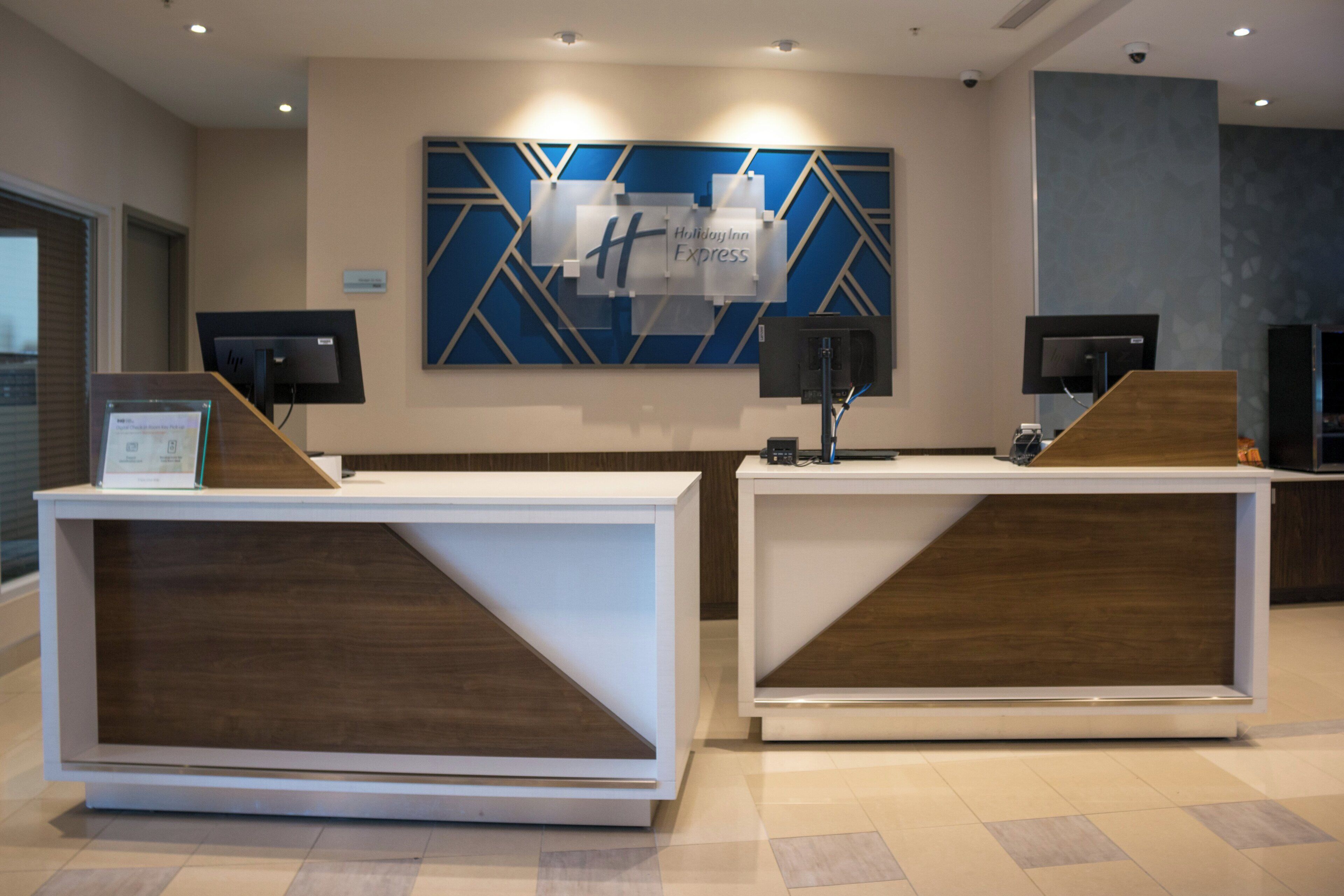 A reception desk area with a modern design, including a blue and white geometric wall art, two reception counters, and a digital screen.