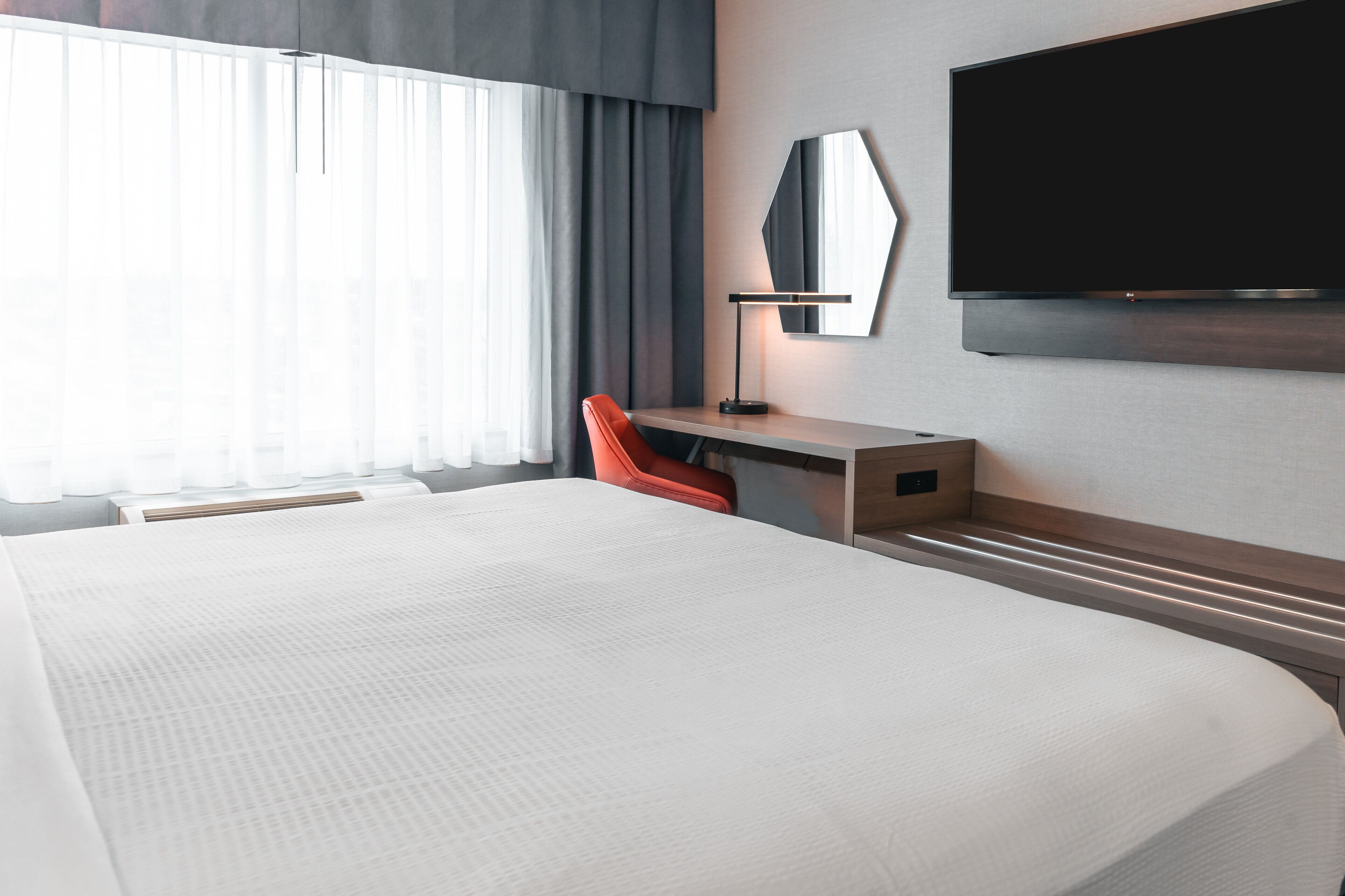 Habitación de hotel con una cama grande, un escritorio con silla, un televisor de pantalla plana y una ventana con cortinas.
