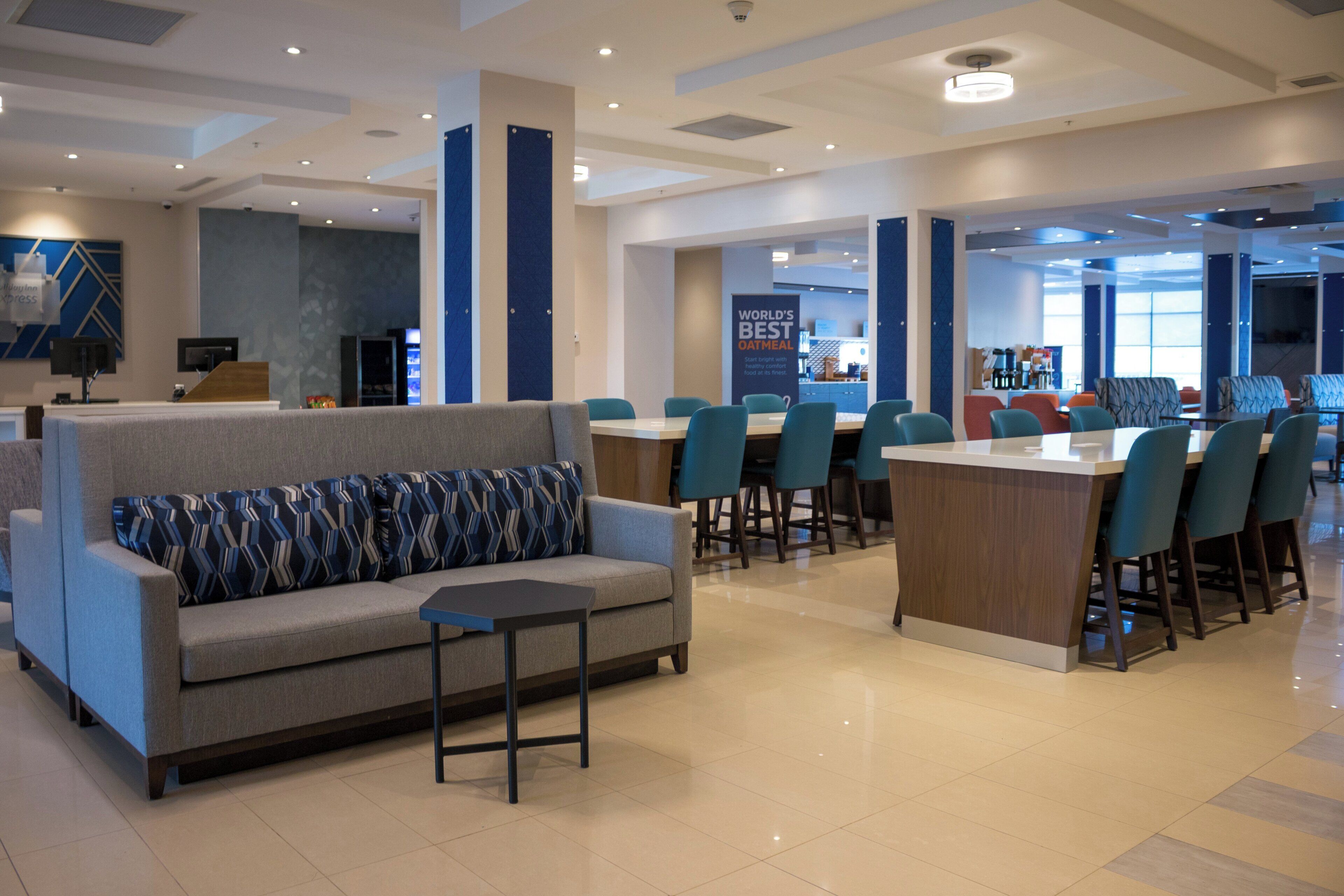A modern hotel lobby with a seating area, a counter, and a view of the kitchen area.