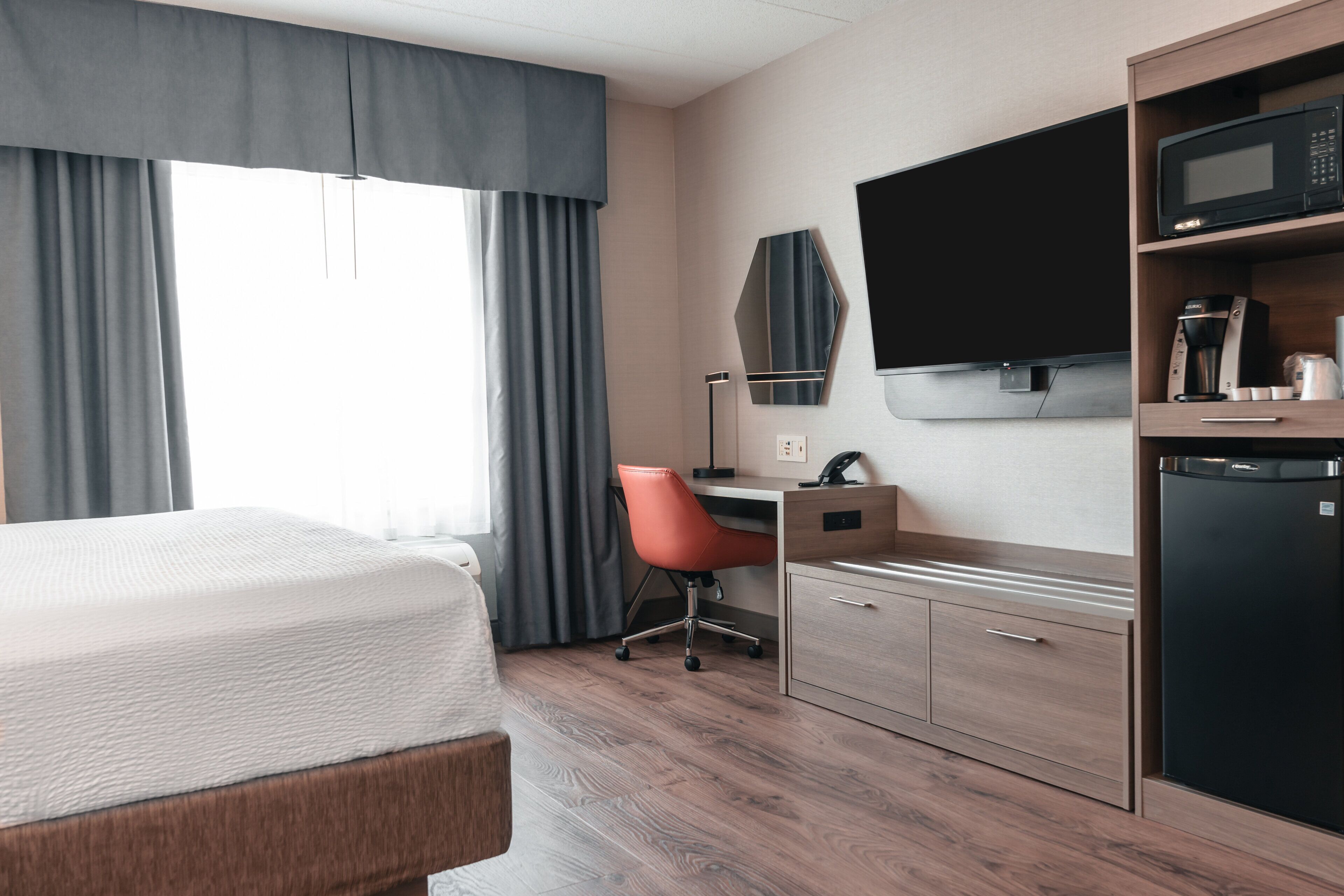 A hotel room with a bed, desk, chair, television, and a coffee machine.