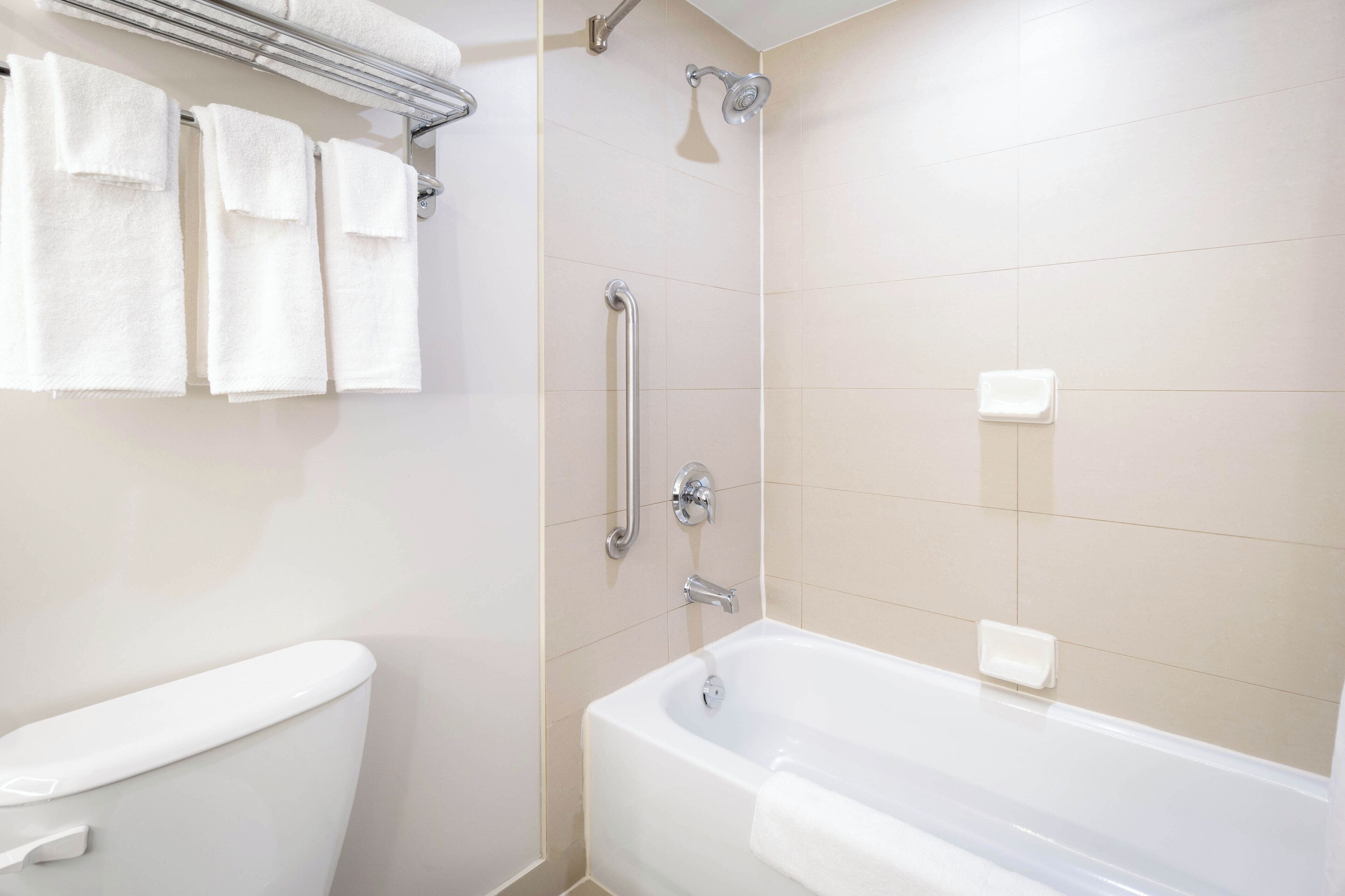 A bathroom with a toilet, a bathtub, and a shower with grab bars.