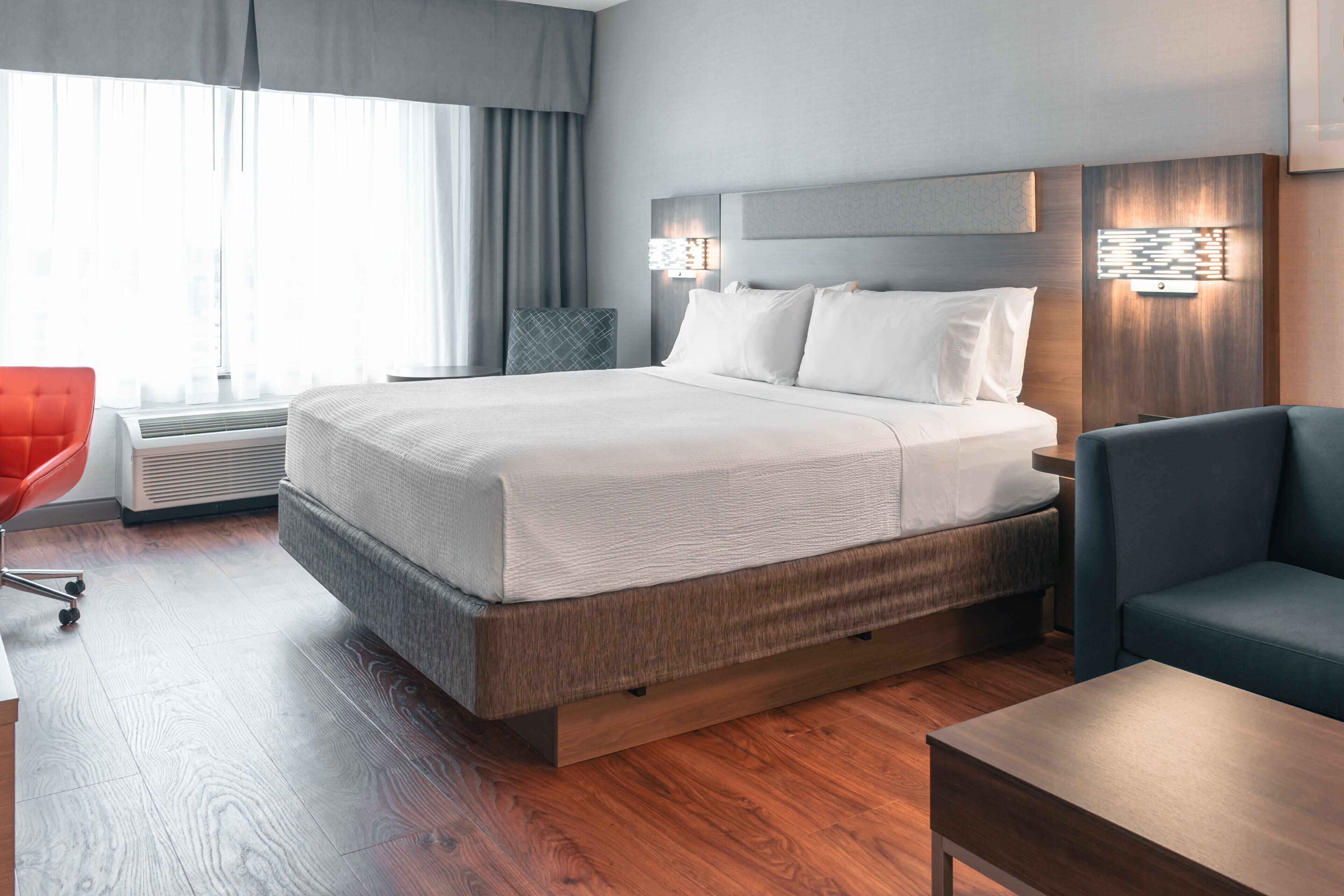 A modern hotel room with a large bed, a desk, a chair, and a heater.