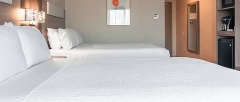 Habitación de hotel con dos camas, una obra de arte colgada en la pared, una mesita de noche, un espejo y una pequeña kitchenette.