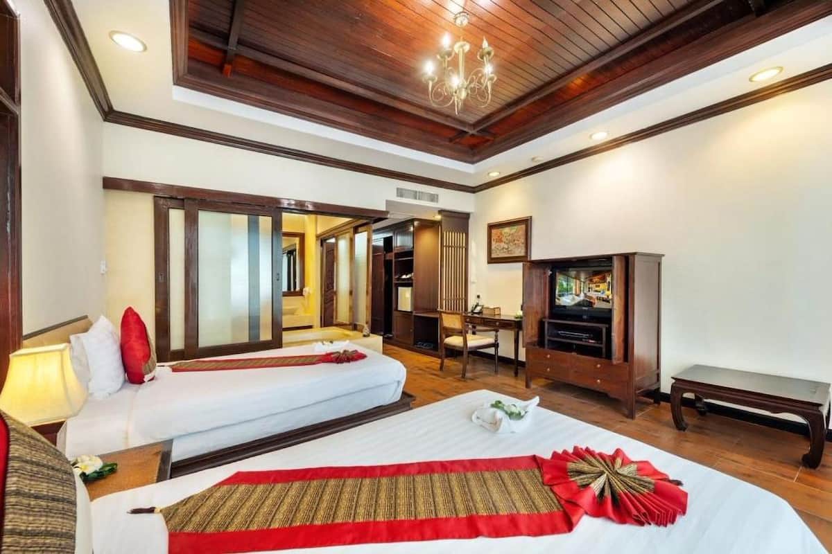 A hotel room with two beds, a desk, a television, and a bench.