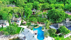 An aerial view of a resort with multiple villas, a central swimming pool, and lush greenery.