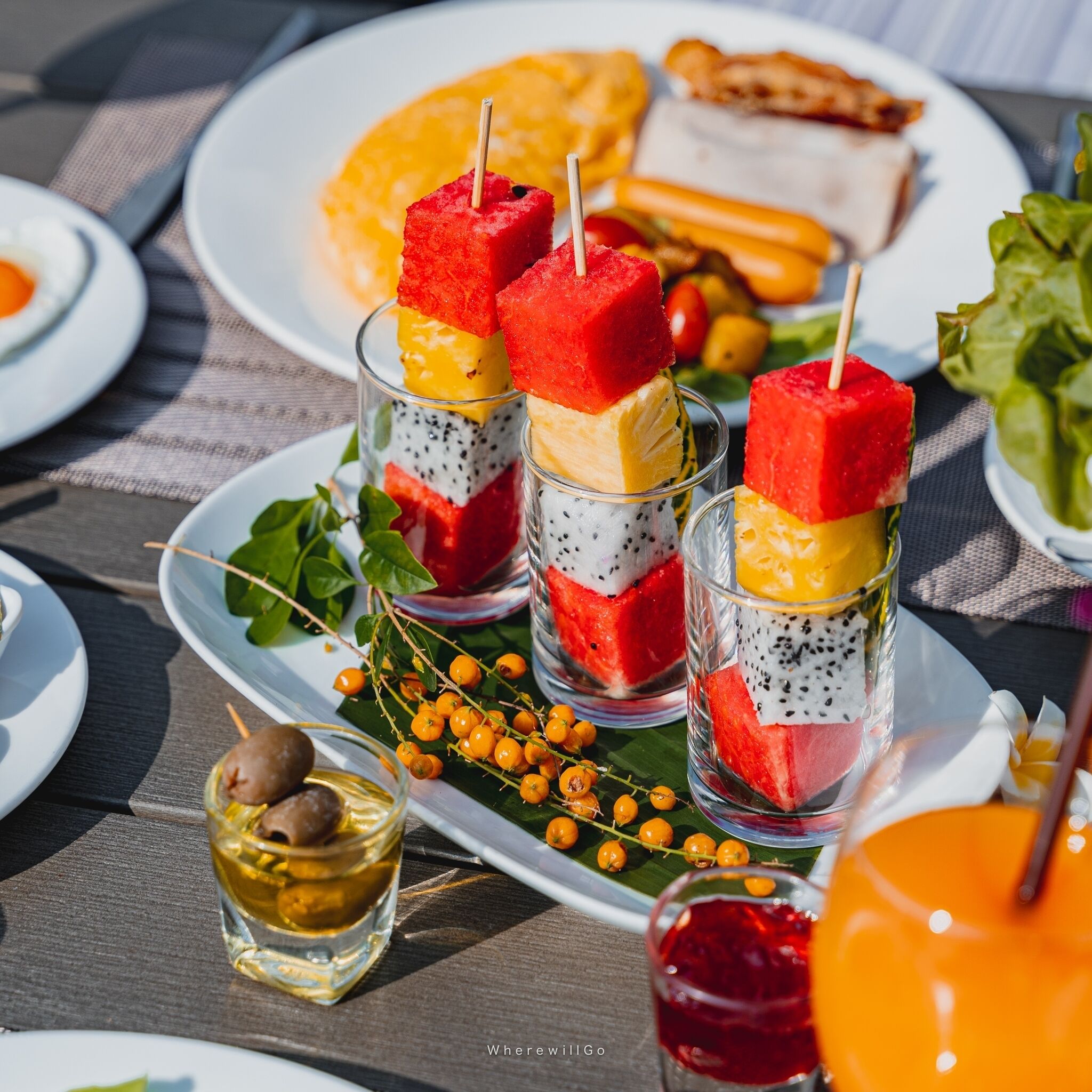 A table with food items including fruit skewers, a plate with bread, and a glass of drink.