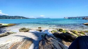 A beach with clear water, rocks, and a pier in the distance.