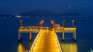A long, illuminated pier extending into calm waters at night, with a mountain in the background.