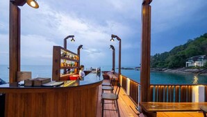 A wooden bar with a view of the sea, a seating area, and a bar counter.