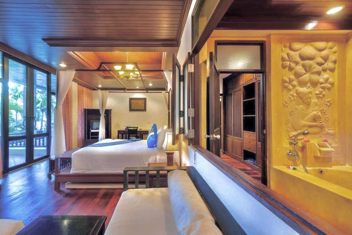 A hotel room with a large bed, a sofa, a desk, and a bathroom with a decorative wall.