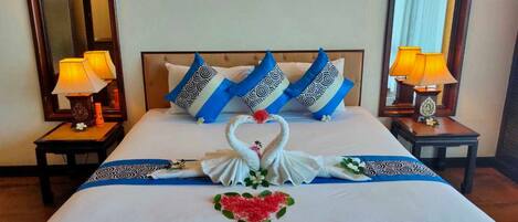 Una cama bien hecha con decoración de cisne y corazón, almohadillas estampadas en azul y blanco y dos lámparas de noche.