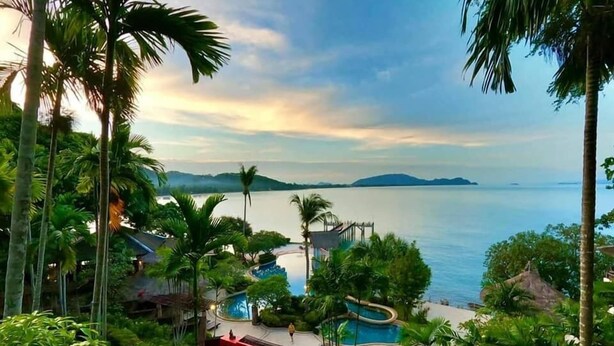A resort with a swimming pool, palm trees, and a view of the sea.