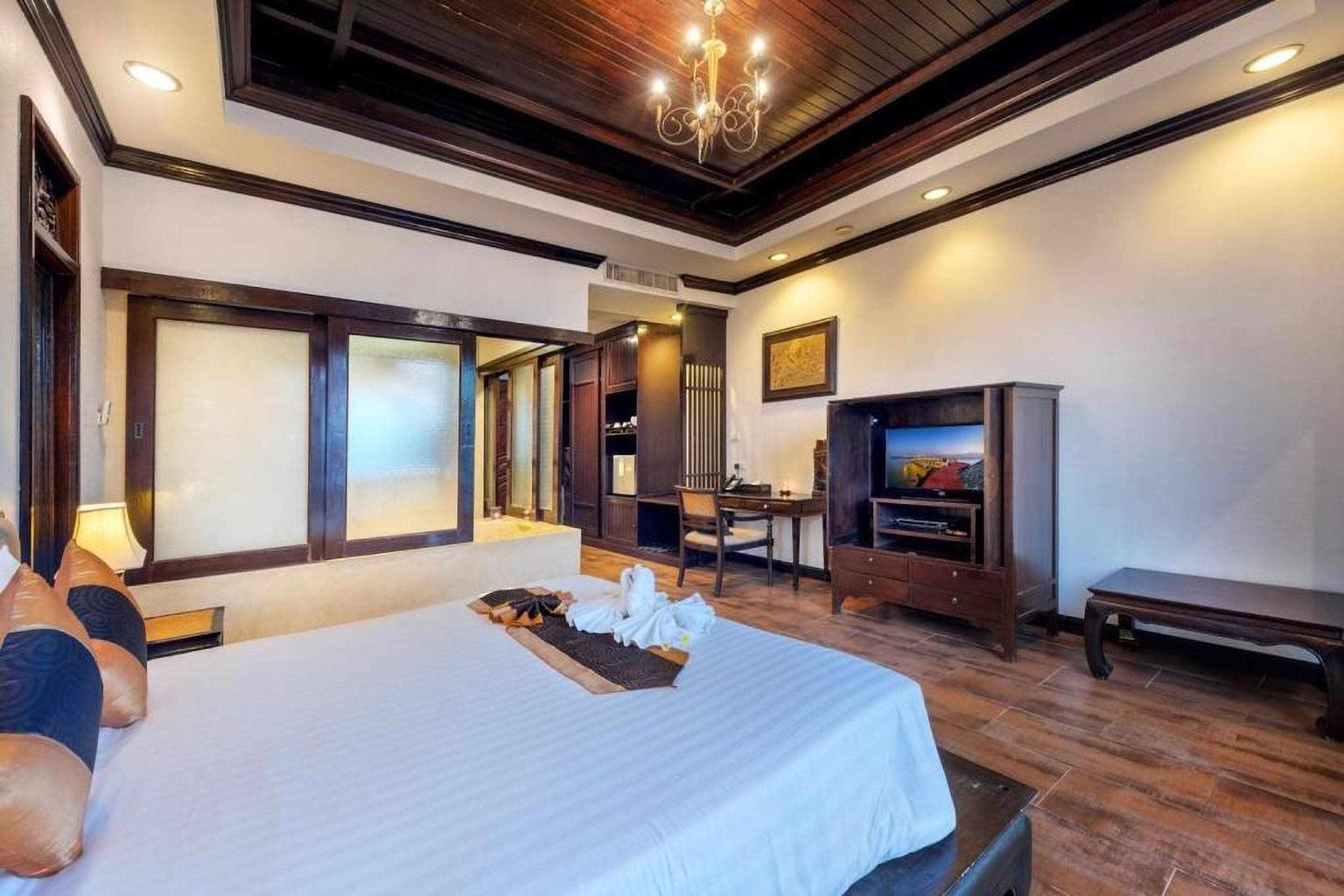 A hotel room with a large bed, a desk, a television, and a bench.