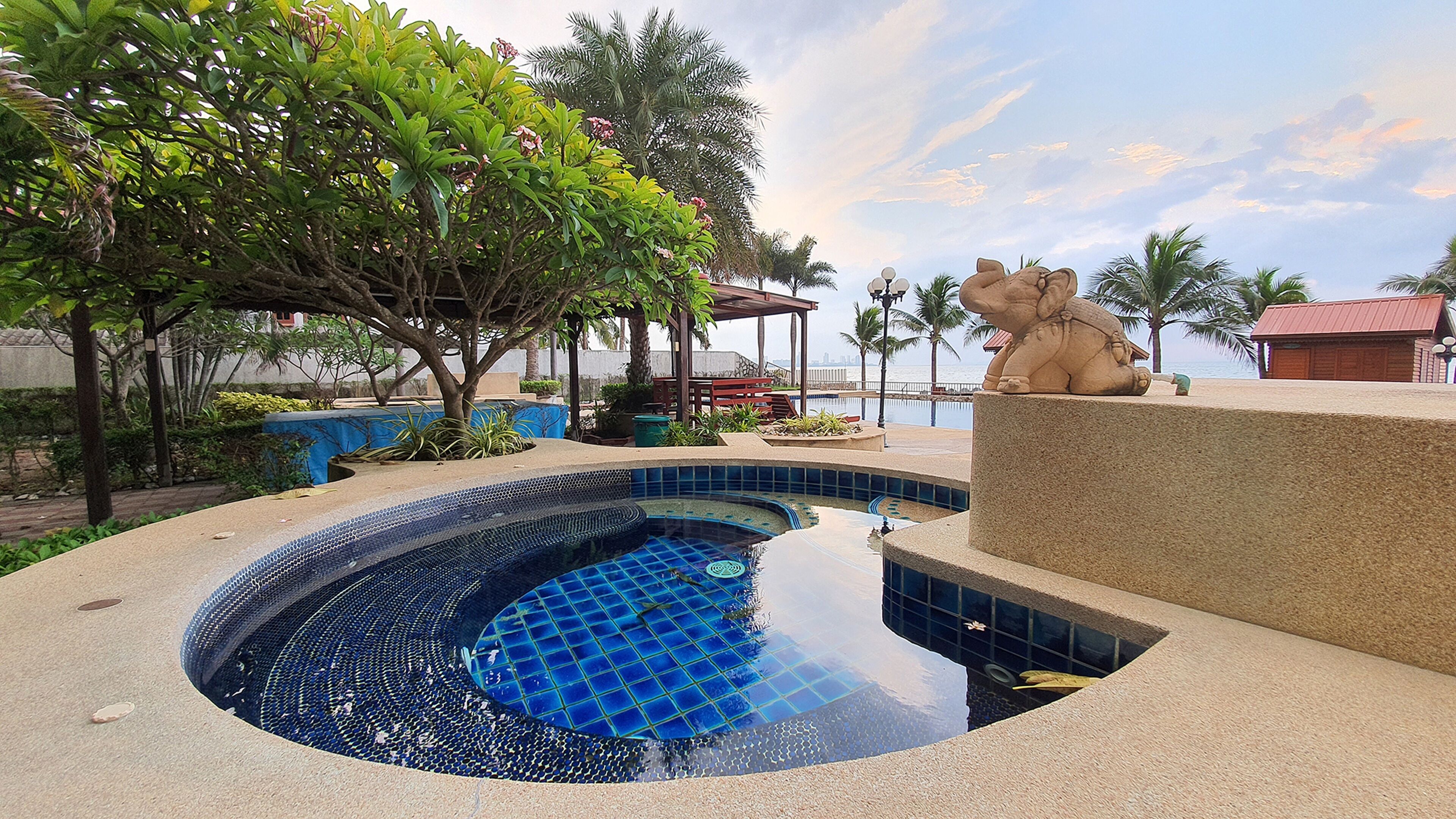 A swimming pool with a unique blue mosaic design, surrounded by palm trees and a statue of an elephant.