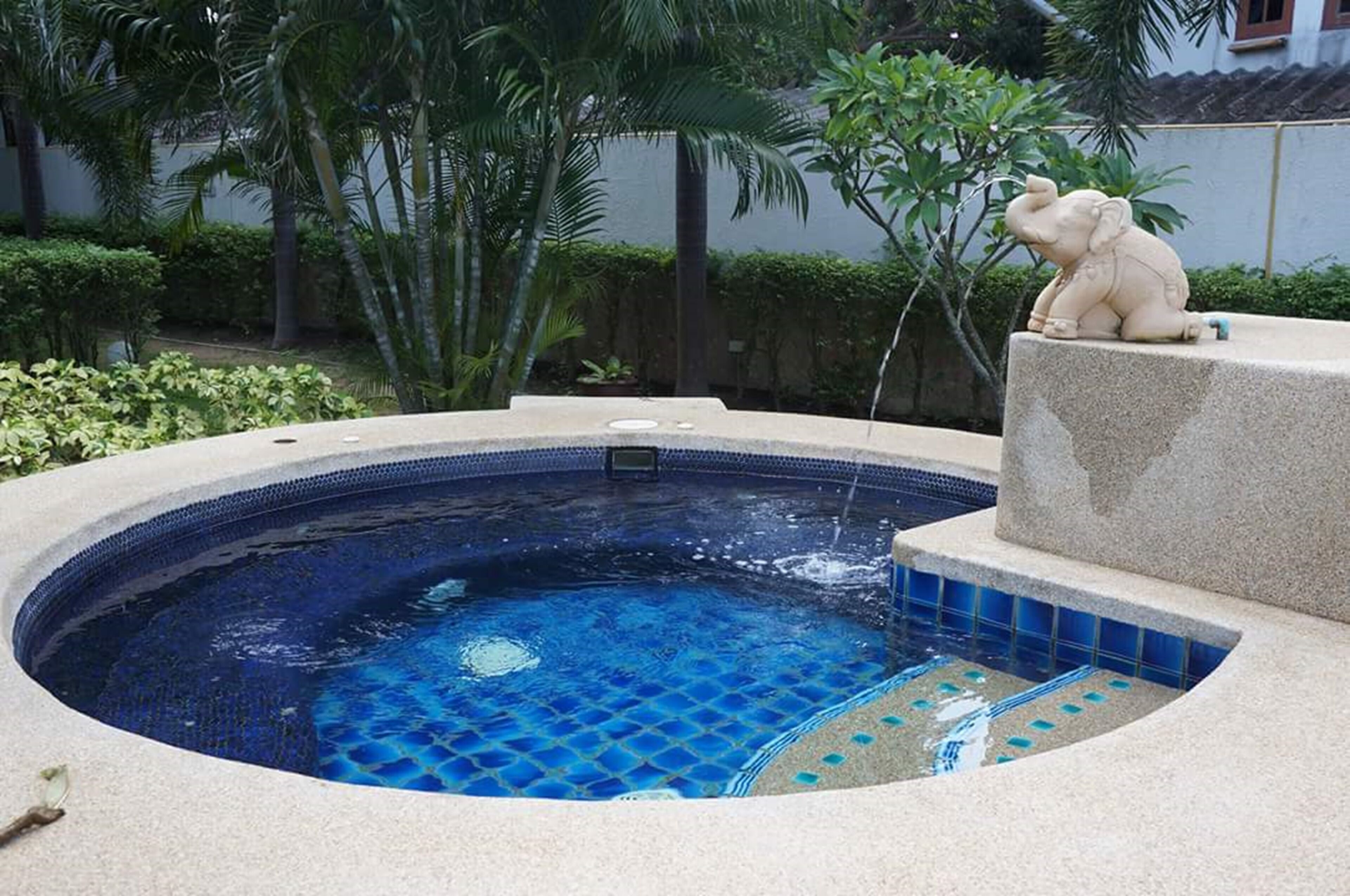 Ein Whirlpool mit blau gefliestem Innenraum, umgeben von einer Steinterrasse und Palmen.