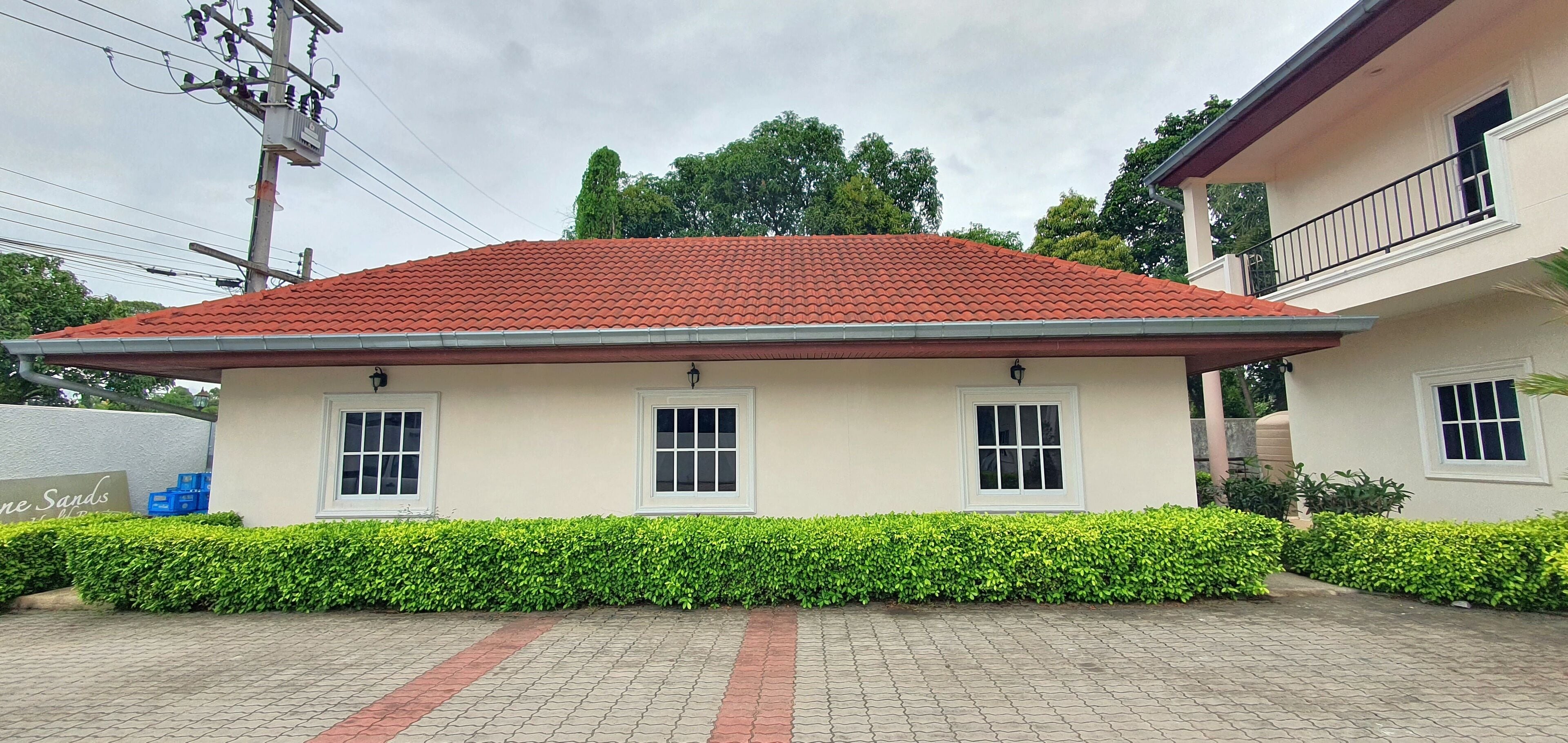 A two-story building with a red-tiled roof, white windows, and a paved driveway.