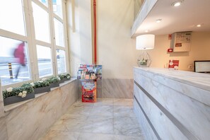 A hotel reception area with a marble floor, a reception desk, a window with a view of the street, and a small plant display. - Hotel do Norte (Porto)