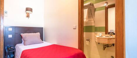 A hotel room with a bed, bedside table, lamp, and a view of the bathroom.