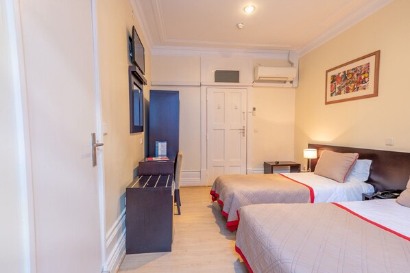 Une chambre d’hôtel avec deux lits, un bureau, une chaise, une armoire et un tableau au mur.