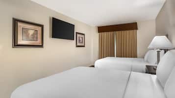 A hotel room with two beds, a flat-screen TV, framed pictures, a window with curtains, and a bedside lamp.