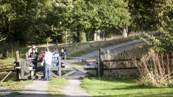 A wooden gate with people standing nearby, a gravel path, and a grassy area with trees in the background.