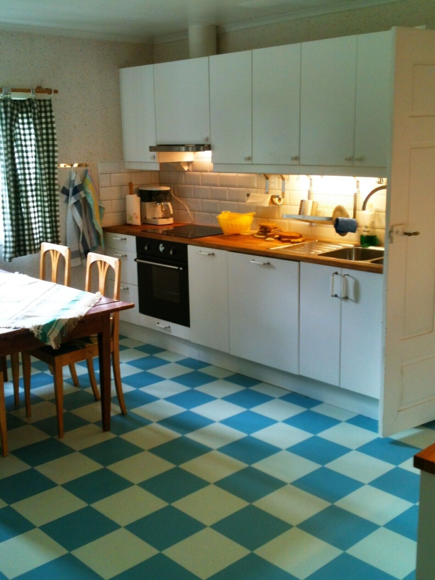 A kitchen with white cabinets, a checkered floor, a coffee maker, and a sink.