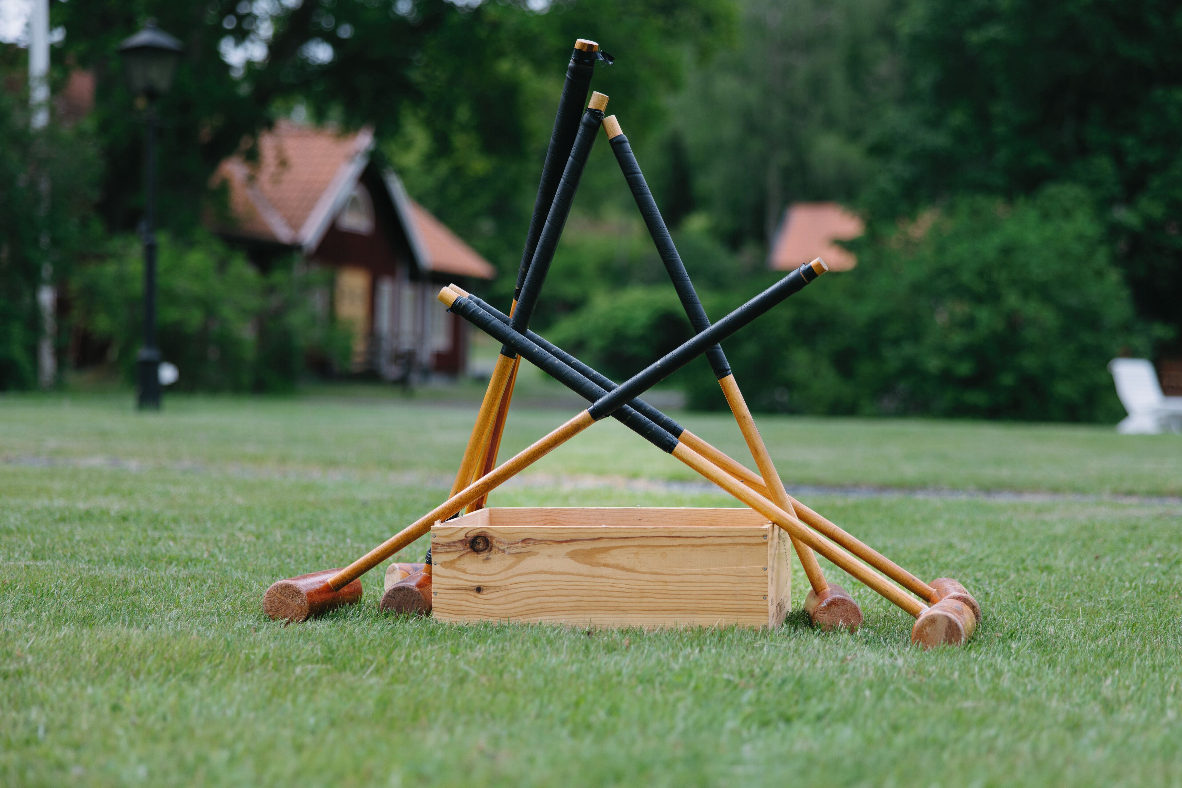 A wooden box with four croquet mallets on a grassy field.
