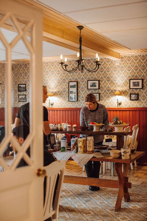 L’intérieur d’un restaurant, avec des poutres en bois, un papier peint à motifs et un lustre.