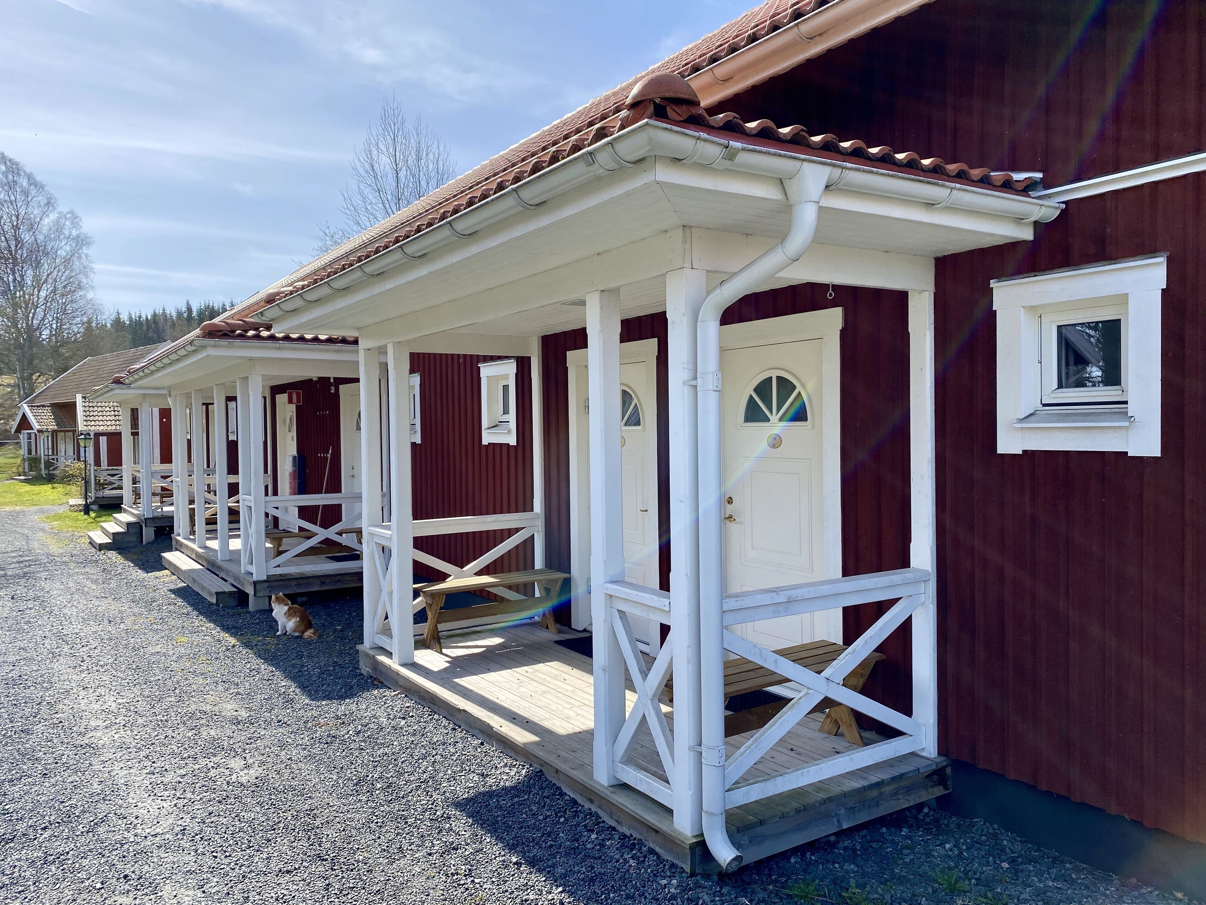 Eine Reihe roter Holzhütten mit weißem Zierstreifen, jeweils mit einer kleinen Veranda und einer Tür mit Fenster.