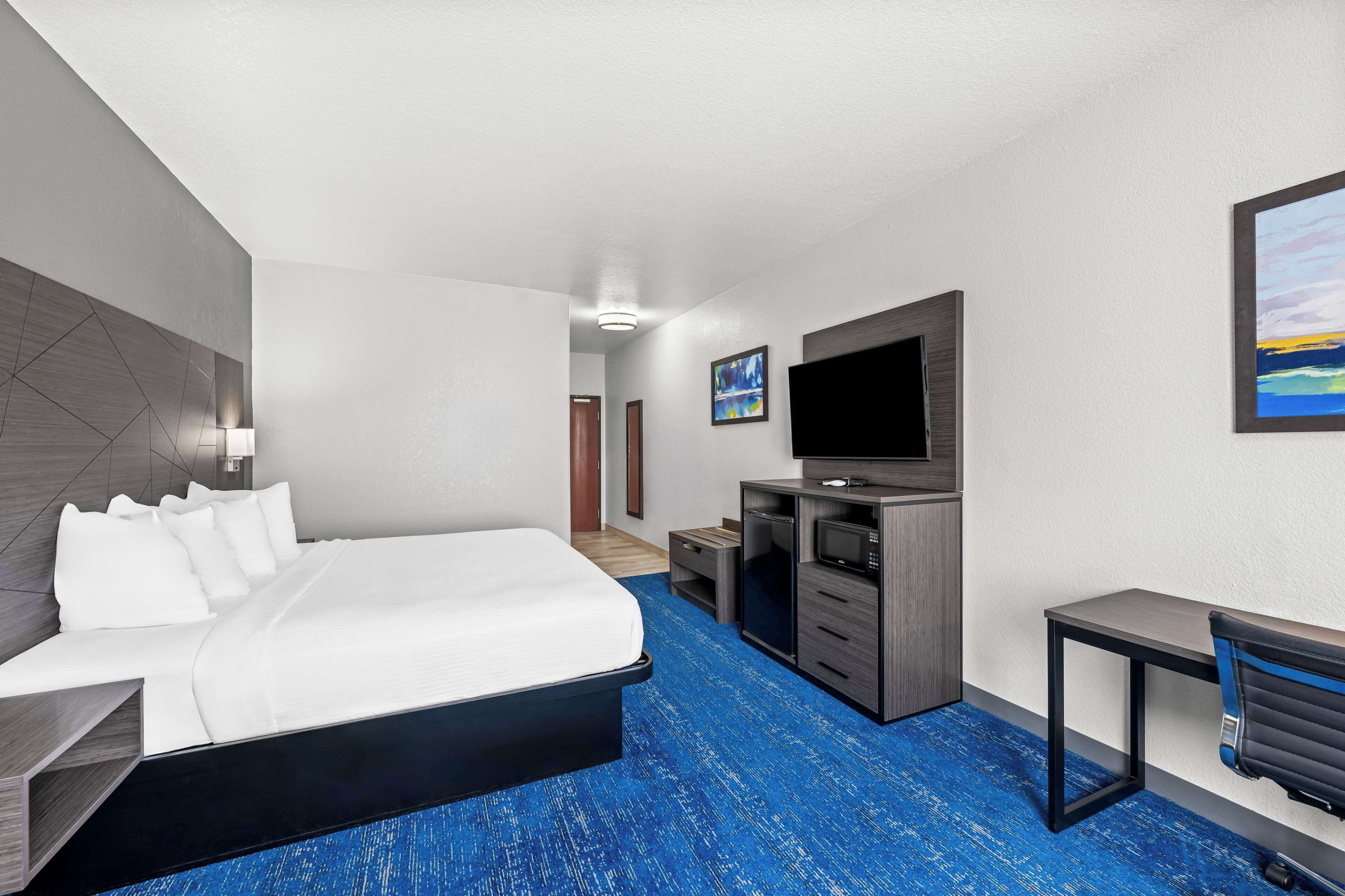 A hotel room with a bed, a desk, a TV, and a painting on the wall.